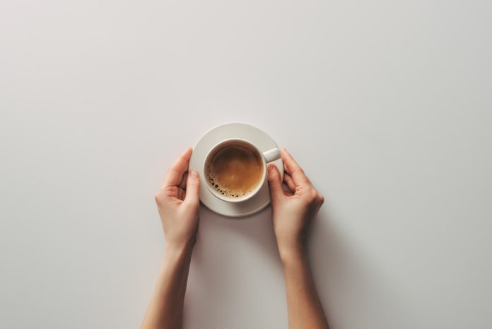 top view of female hands and cup of coffee with saucer on grey caffè