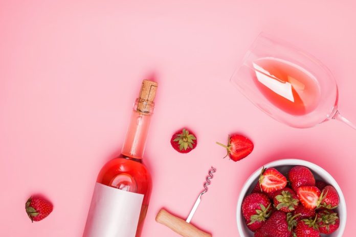 fragole al vino fragole al vino; bottiglia di vino rosso e ciotola di fragole su sfondo rosa